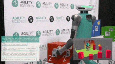 Digit, with a teal torso and grey appendages, is seen manipulating a red box near a labeled tower, illustrating its capability to interact with objects following programmed instructions.