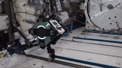 A robot  moves on striped flooring in a spacecraft setting.